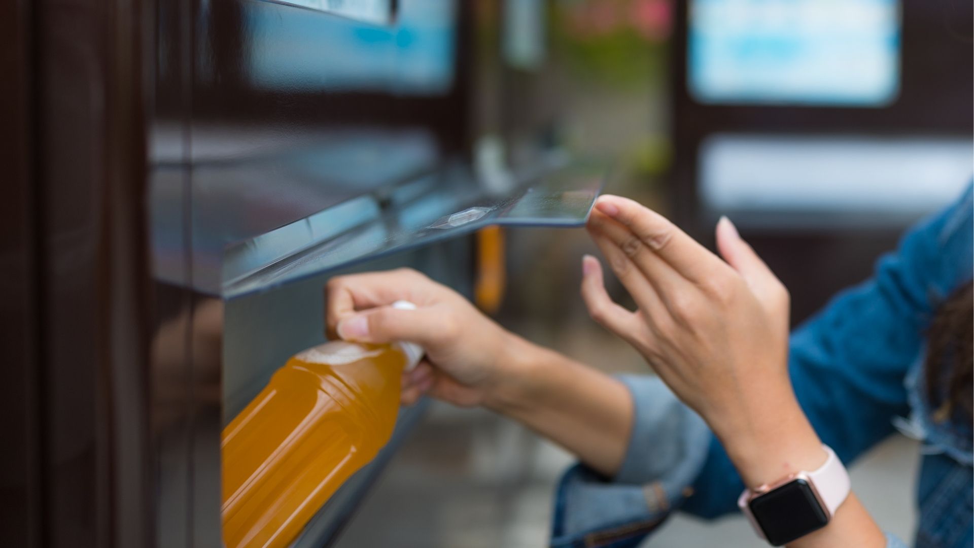 A woman is picking up bottle from vending machine